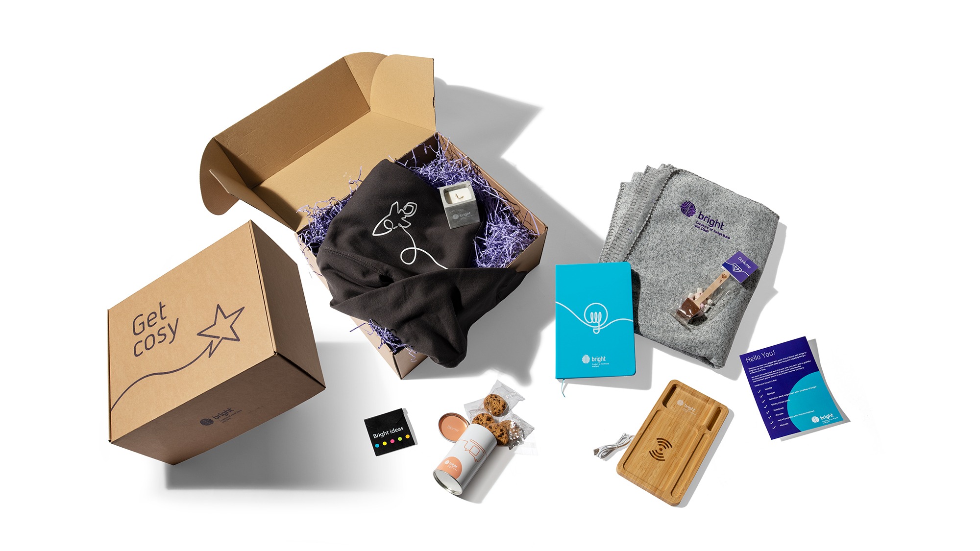 Flat lay image of a swagpack box, including a black hoodie, wooden phone charger, plant-in-a-pot and hot chocolate on a stick