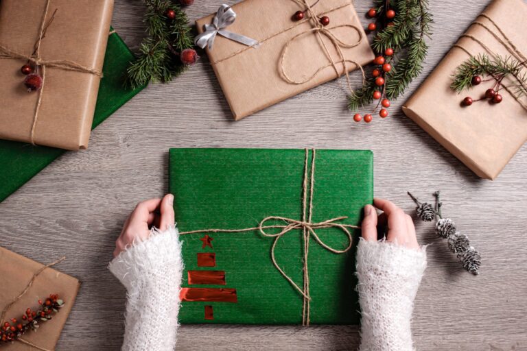 Gift wrapped in green paper and brown string with a red foil Christmas tree decoration