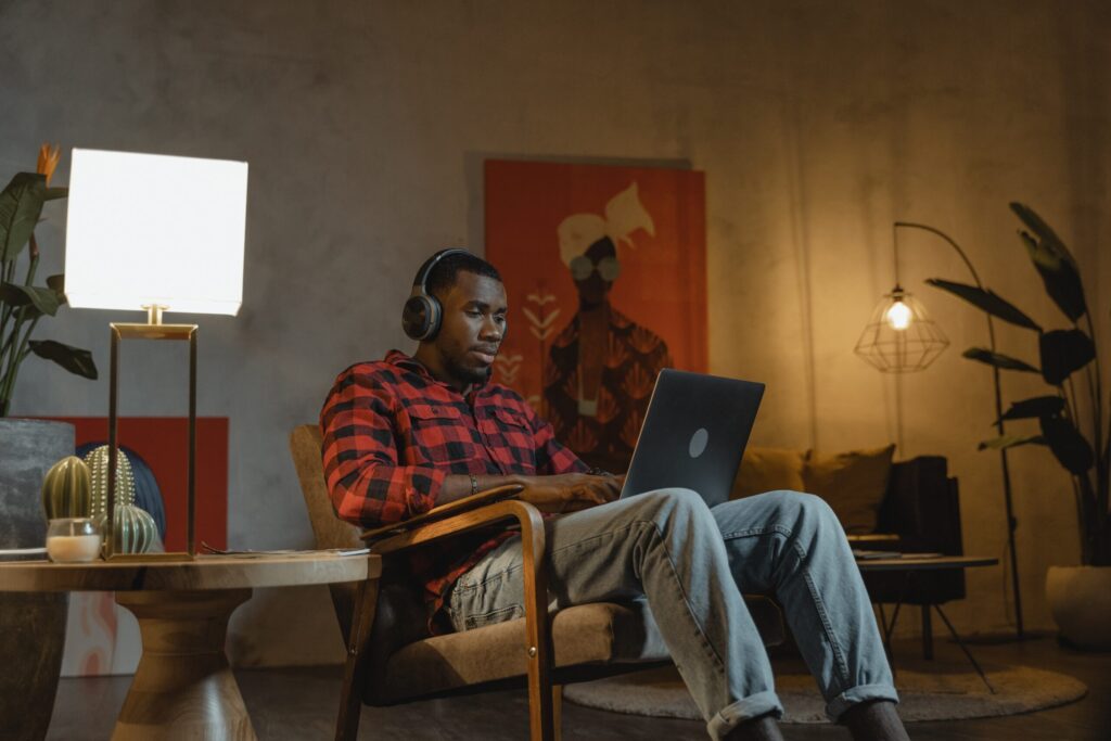 A young man sat in his living room wearing headphones and working with a laptop on his knees