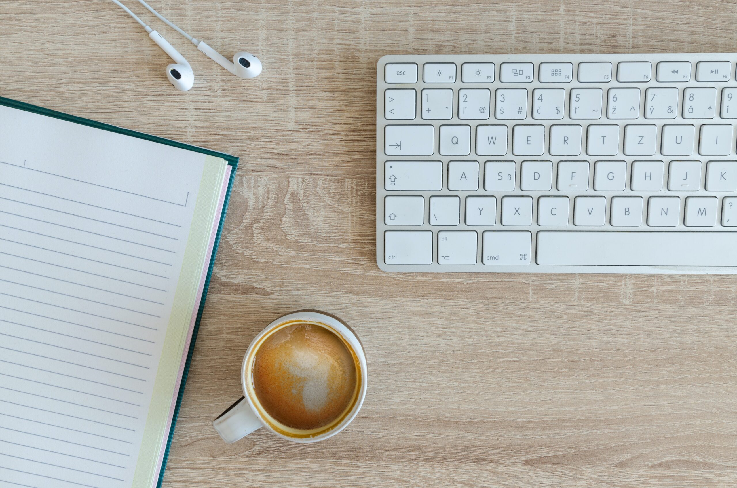 Coffee, keyboard, notebook, and headphones on a wooden desk backdrop